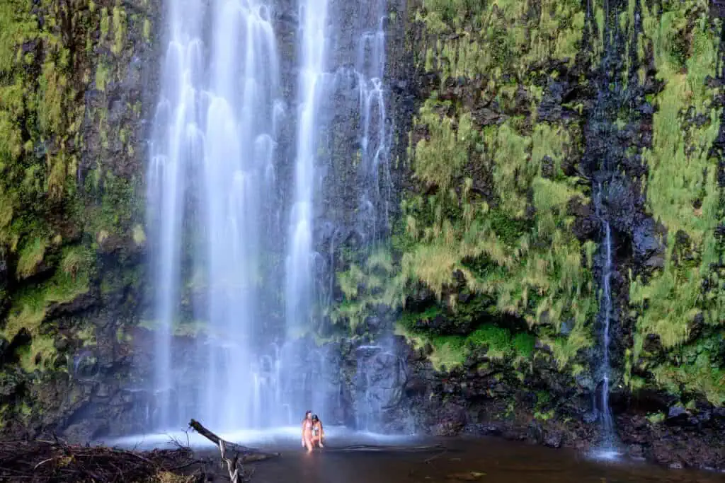 Two people standing under large waterfall